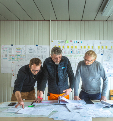 Trois collaborateurs Mobility analysent des plans techniques sur une table de travail.