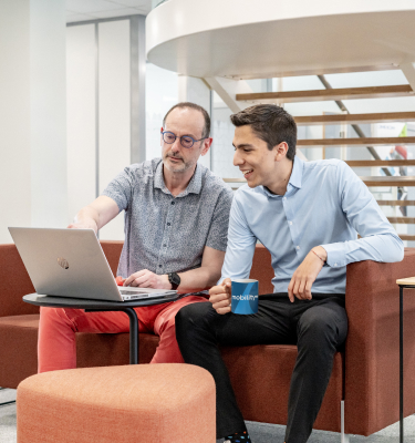 Deux collègues discutant autour d'un ordinateur portable dans un bureau moderne.