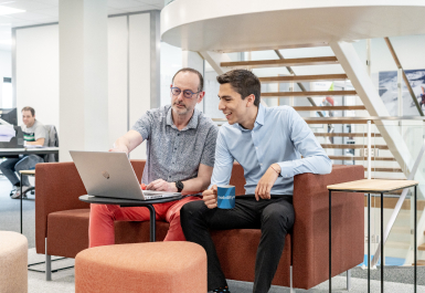 Deux collègues discutant autour d'un ordinateur portable dans un bureau moderne.