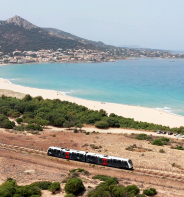 Un train traverse un paysage côtier en Corse, longeant la plage de Calvi