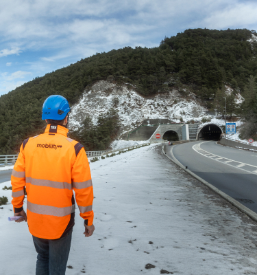 Un collaborateur Mobility, équipé d’un casque et d’un gilet de sécurité, se dirige vers une infrastructure routière enneigée, à proximité du tunnel du Fréjus.